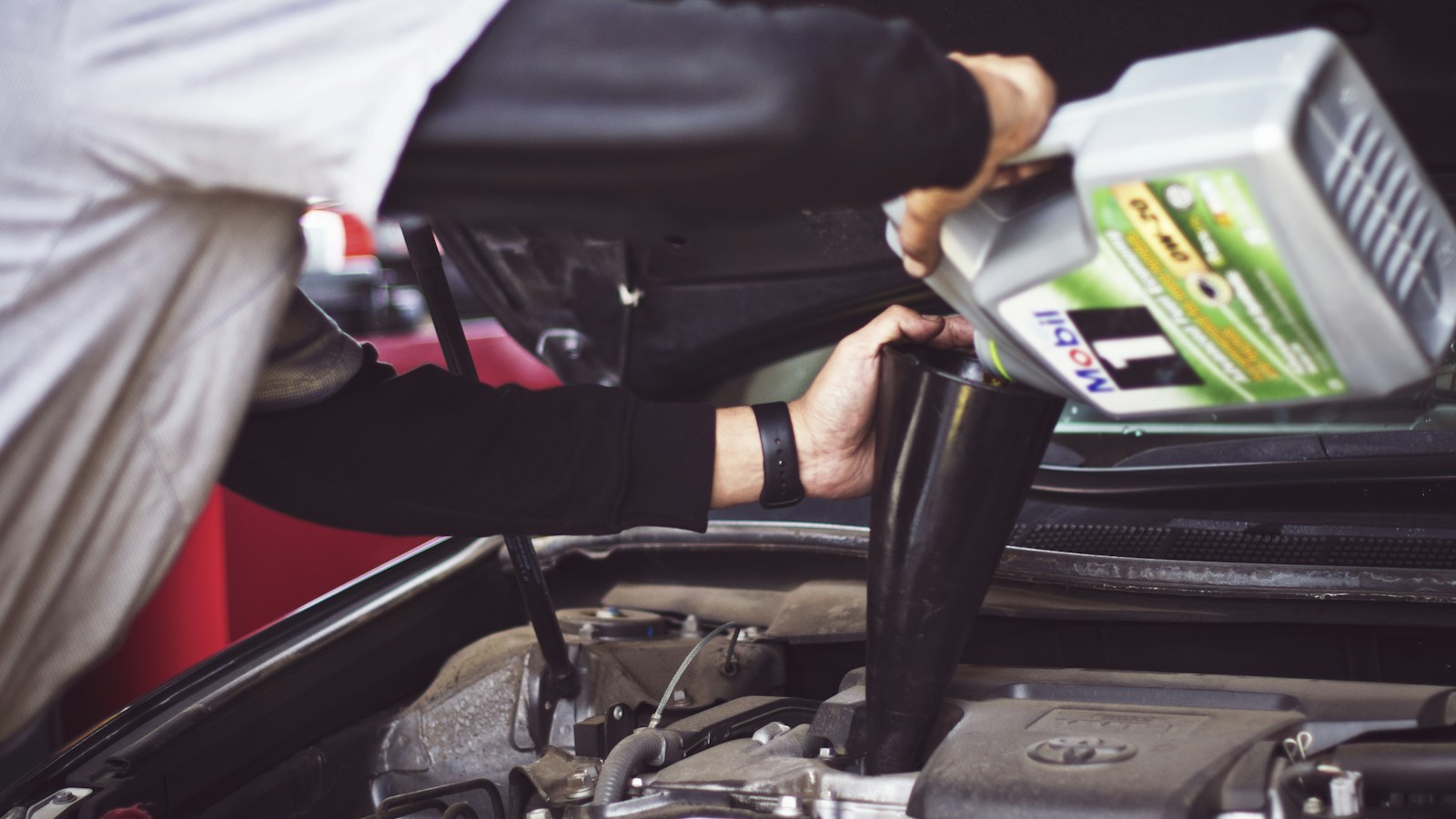Motor kaputu açık bir araca huniyle motor yağı dolduran kişi